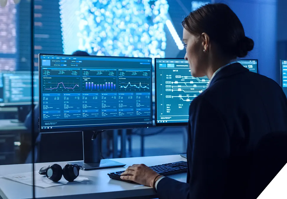 Imagen generada por IA de una profesional de espaldas trabajando en un entorno de centro de control, supervisando múltiples monitores con gráficos de datos y métricas complejas en tiempo real.